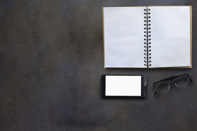 Directly above shot of open book with smart phone and eyeglasses on table