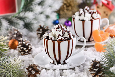 Hot chocolate with marshmallows in a white ceramic mug, with tangerines on a snowy table.