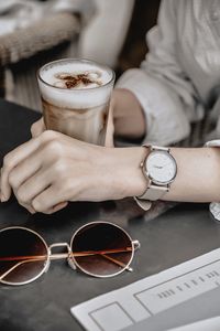 Midsection of person having coffee in glass at table