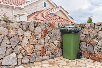 Green garbage bin next to the house on back yard