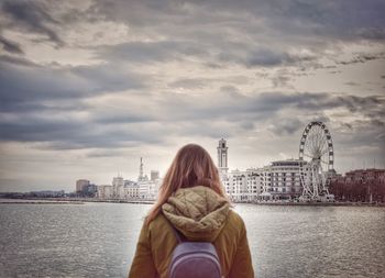 Rear view of woman looking at cityscape against cloudy sky