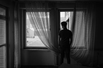 Rear view of man looking through window at home