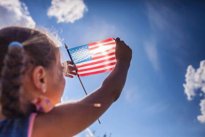 Low angle view of man holding flag against blue sky