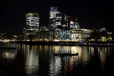 Illuminated buildings by river against sky at night