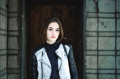 Portrait of young woman wearing jacket while standing against wall