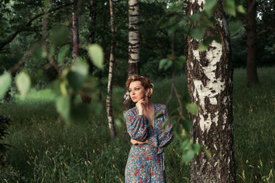 Young woman standing by tree trunk in forest