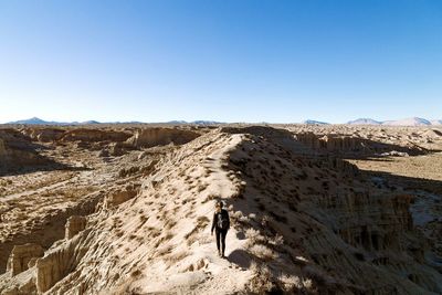 Rear view of woman walking on desert against clear sky