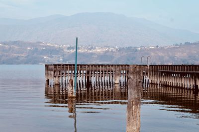 Wooden posts on pier over lake against sky