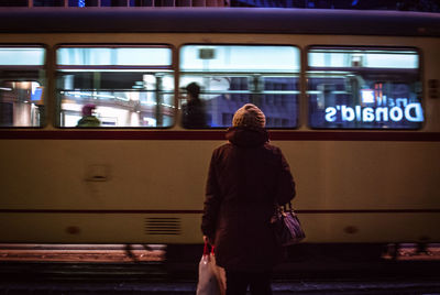 Rear view of woman standing against moving bus at night