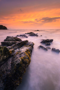 Rocks by sea against sky during sunset