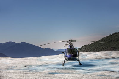 Helicopter landing on snowcapped mountain against sky