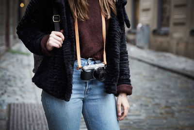 Midsection of woman with camera standing in alley at city