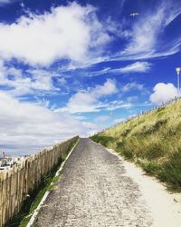 Empty road amidst field against sky