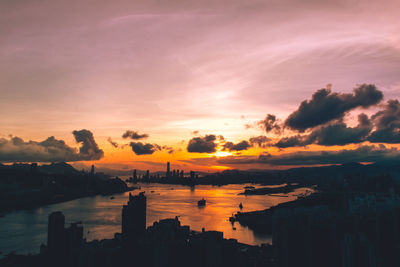 Silhouette buildings by sea against romantic sky at sunset