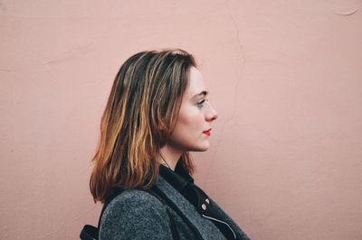 Side view of young woman against pink wall