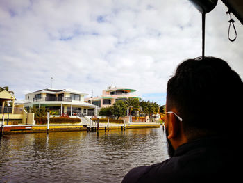 Rear view of man on boat in river against cloudy sky