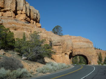 Road by rock formation against clear blue sky