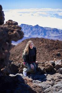 Young woman sitting on rock against mountain