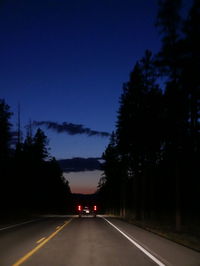 Road amidst silhouette trees against sky at night