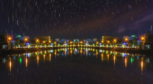 Illuminated buildings by river against sky at night