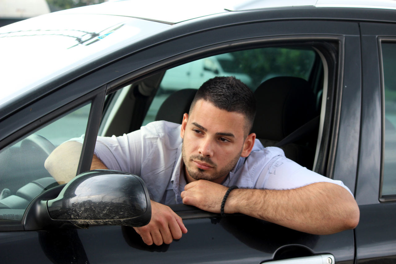 PORTRAIT OF YOUNG MAN SITTING BY CAR