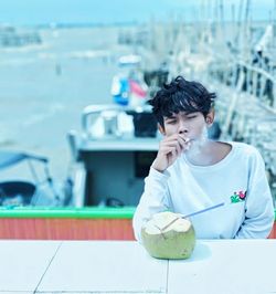 Young man looking away while sitting on table by sea