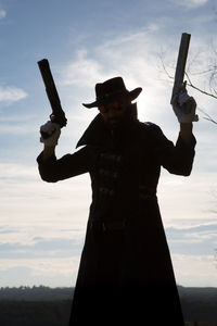 Man with arms outstretched standing against sky