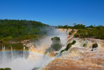 Scenic view of waterfall in forest against clear sky