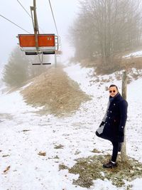 Portrait of young man standing on snow with ski lift in the background