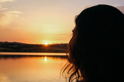 Close-up of young woman by lake against orange sky