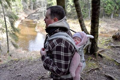 Side view of father carrying baby daughter while walking in forest