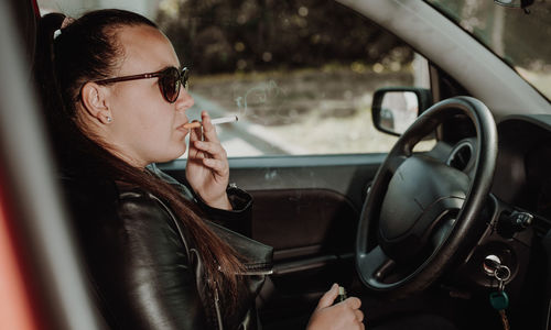 Portrait of young woman holding cigarette in car
