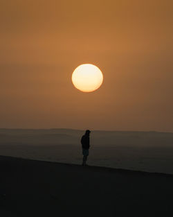 Silhouette man standing at beach against sky during sunset