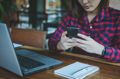 Midsection of woman using smart phone on table