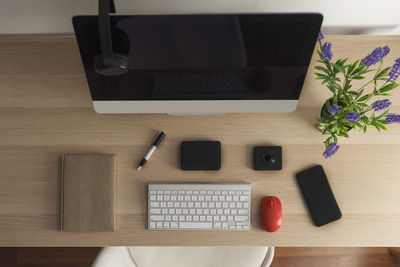 Overhead view of a workspace. we can see a computer, a smartphone, a notebook,, headphones, a keyboard, a pen, a red mouse, a plant, a 360-degree camera and a hard drive.