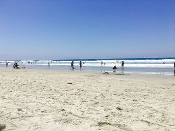 People on beach against clear blue sky