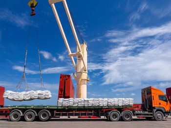 Low angle view of crane picking packages against blue sky