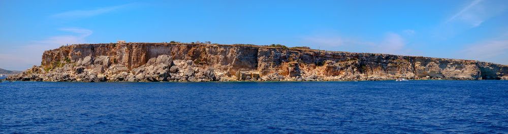 Rock formations by sea against blue sky