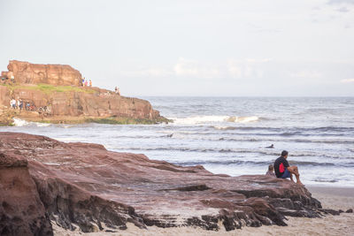 Man standing on cliff by sea against sky