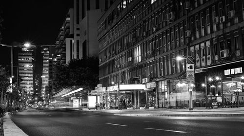 Illuminated street amidst buildings in city at night