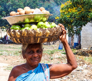 Portrait of smiling senior woman carrying fruits in basket in city