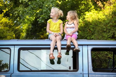 Two girls sitting on top of roof of vintage car in summertime