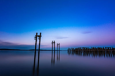 Wooden posts in water against sky at sunset