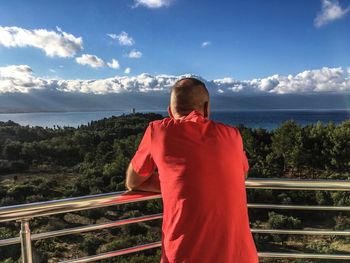 Rear view of man standing by railing against sky