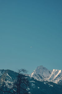 Low angle view of snowcapped mountains against clear blue sky