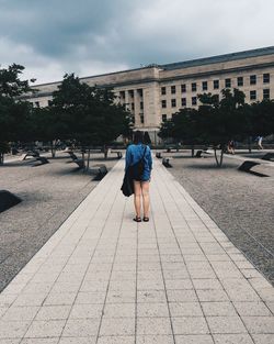 Full length rear view of woman standing footpath by building against sky