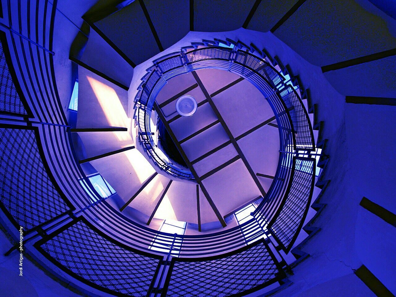 indoors, low angle view, built structure, ceiling, architecture, pattern, spiral staircase, circle, directly below, design, staircase, blue, spiral, steps and staircases, steps, geometric shape, skylight, railing, modern, architectural feature