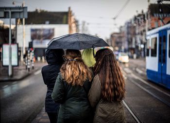Rear view of female friends with umbrella walking on city street during monsoon