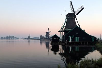 Traditional windmill by water against clear sky