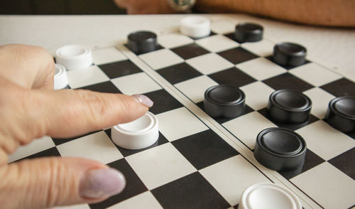 A woman's hand moves a white checker on a black-and-white playing field, the concept of hobbies 